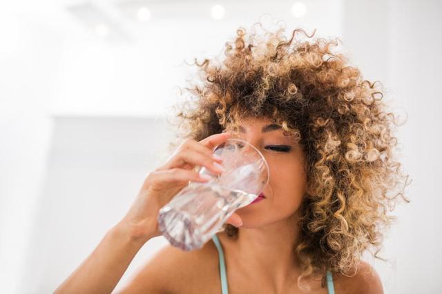 African woman in the middle of drinking a glass of water