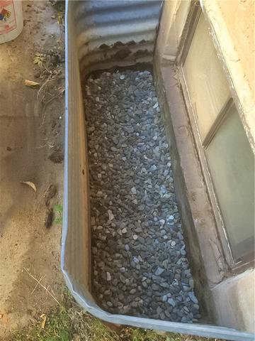A view of the window well on the exterior of the home during the WellDuct® installation after drainage gravel rock has be placed back. You would never know the system is even there!