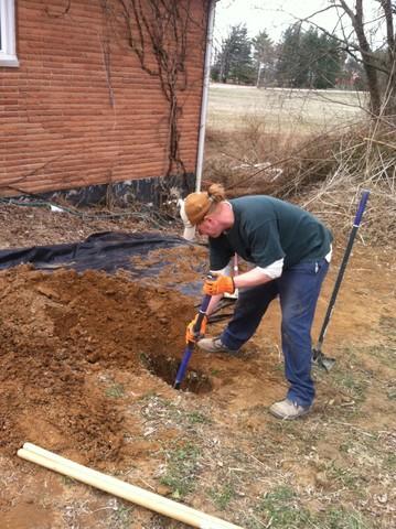 <p>Here, the installation crew member is securing the earth anchor while the wall anchor rod is being driven into the earth. This way, he insures that the earth anchor will meet up with the wall anchor rod with no problems. Once that is secure, he will refill the hole with the dirt on his left and tamp it properly.</p>