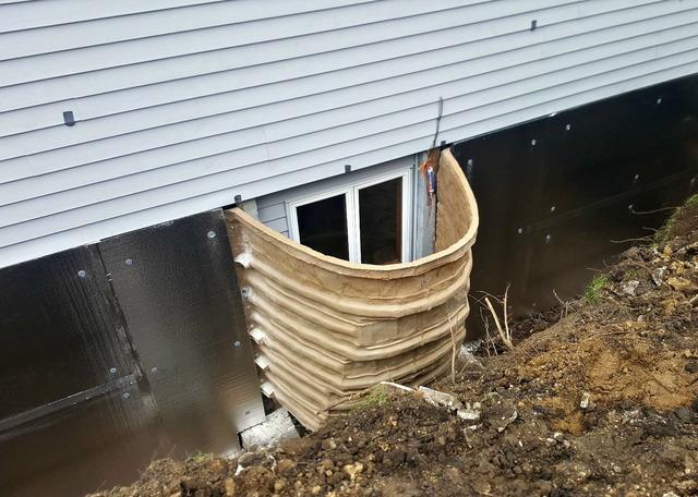 The soil surrounding the home has been removed to install the RockWell Egress Window Well and the wall anchors. SilverGlo has been installed externally on the foundation to prevent moisture from seeping in and to help insulate the basement.