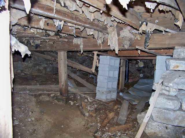 The homeowners attempted to fix the problem of rotting support beams in the Gilman, CT crawl space by creating columns made of concrete blocks. These are short term solutions that do not fix the long term problem of a sagging crawl space. The thick, heavy columns will continue to sink into the earth below as the weight of the house pushes down on them. More shims, the wooden planks above the blocks, will need to be wedged in as the columns sink, and the "solution" will ultimately fail. 