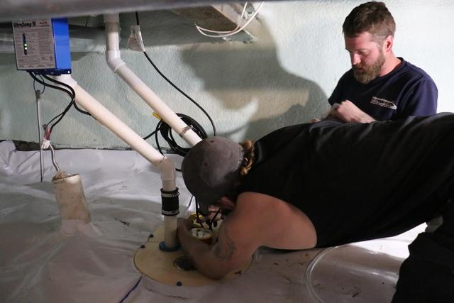 Advanced Basement Systems crew members put the finishing touches on the Triple Safe Sump Pump System.