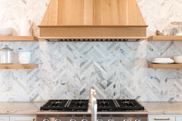 Custom hood with a natural wood finish and beautiful chevron tile backsplash design.