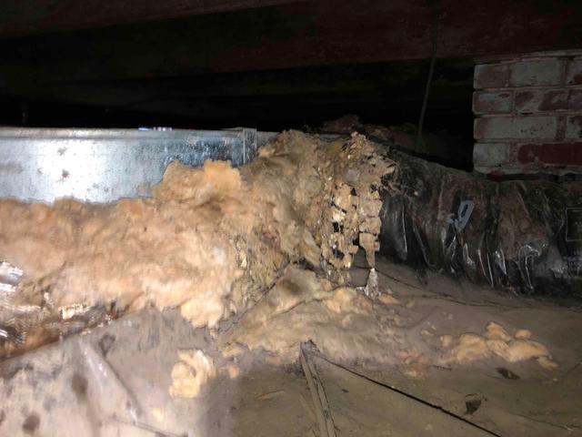 Fiberglass insulation has fallen out of the floor joists and deteriorated in this crawl space. The fiberglass acts as a sponge, absorbing moisture from the crawl space air and sagging out of position. Water droplets pull apart the fine glass fibers and gravity pulls the heavy insulation downwards, rendering it useless.