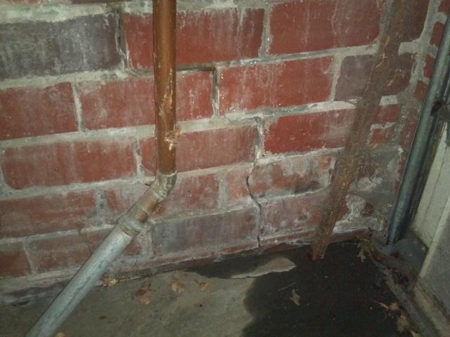 <p>The stair step cracks in grout of this brick wall shows a twist in the foundation. In addition, the foundation is leaking water. This water is coming in at the floor joint where the wall, footing, and floor all come together.</p>