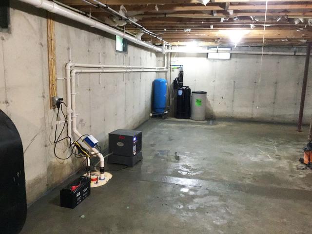 This is a wide-angle of the basement, showing where the sump pump was installed within the basement, and where other basement equipment is stored.