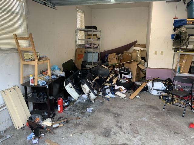 Before - car parts, chairs, small furniture and boxes are scattered throughout the garage.