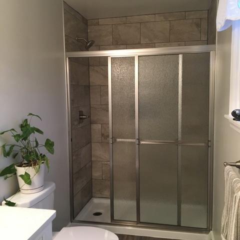 View of a new walk-in shower, glass doors, and wall tile