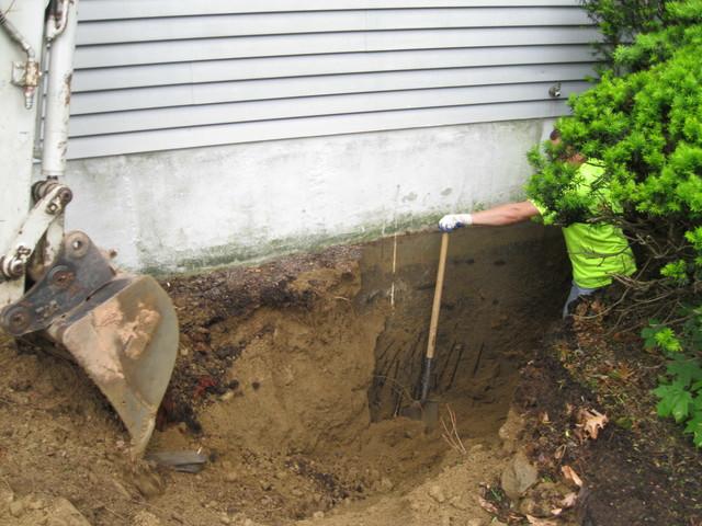 To install a push pier system, soil is first removed to expose the foundation footing where the pier will be driven.