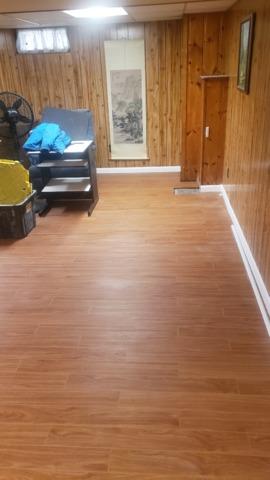 The Thermal Dry Elite Plank Floors have been installed, and are glowing under the overhead lights in this basement. They give the old wood paneling a modern look.