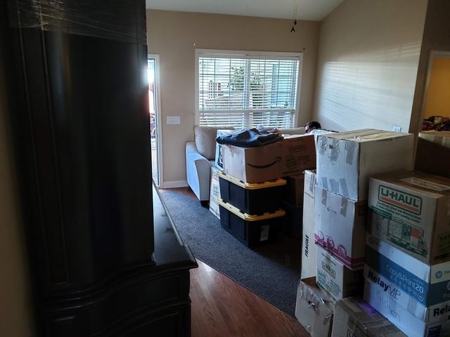 This is the back living room, complete with the large entertainment center (large dark piece taking up the left side of the picture), sofa, and a comfy chair, and many boxes, moving blankets, etc.