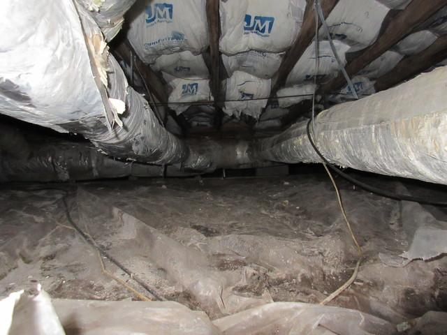 Looking in crawlspace down at vapor barrier and duct work