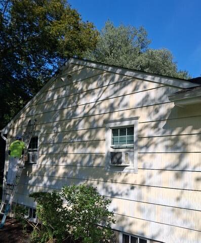 Our crew actively scraping, sanding, and prepping the wood siding on ladders to ensure maximum paint adhesion.