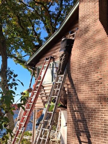 Professional contractors utilizing multi-ladder extension setups to reach difficult, high-elevation brick chimney trim and log siding safely.