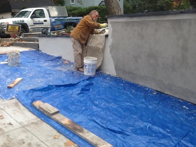 Dana is coating the wall. Here you can see the measures we take in protecting the driveway from droppings of coatings or parging.