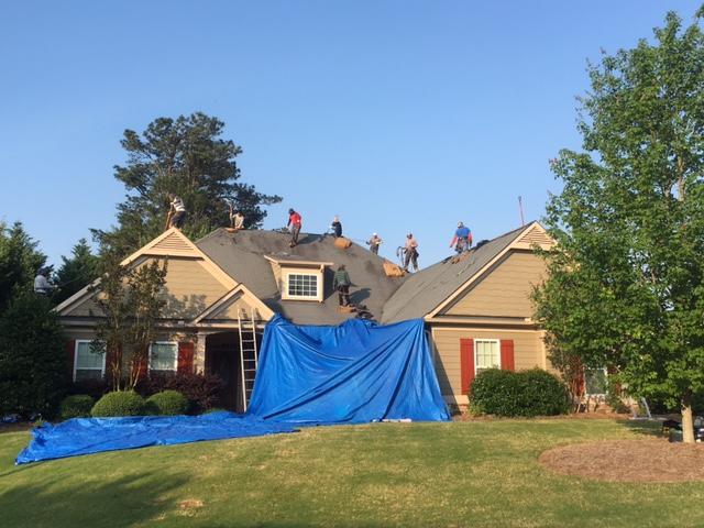 This picture shows how are crew took the time to protect this customer's large Japanese maple tree and flowers by using decking sheets underneath the blue tarp. Also, this picture shows the crew beginning to remove the ridge shingles