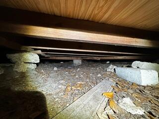 The crawl space lacks proper support, as the block piers and makeshift support structures have settled into the ground, resulting in sagging floor joists above.