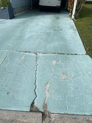 The homeowner's driveway has settled significantly due to major soil erosion, resulting in large cracks forming in the concrete slabs.