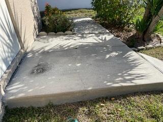 Soil erosion beneath the homeowner's walkway has led to cracking and settling of the concrete, resulting in an uneven surface.