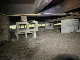The original block piers in the crawl space have settled into the soil below, resulting in inadequate support for the floor joists above.