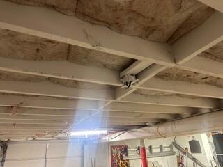 This photo shows signs of structural stress in the home's floor system. The added support beam suggests the original joists were sagging or failing, likely causing uneven floors above. The aged insulation and sealed wood indicate past moisture issues, which can lead to musty odors, mold, and poor air quality. Together, these symptoms point to a crawl space or basement that was experiencing both structural instability and excess humidity.