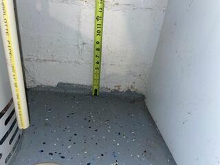 A tape measure reveals previous water line marks on the basement wall, showing just how high moisture levels had risen before the waterproofing system was installed.