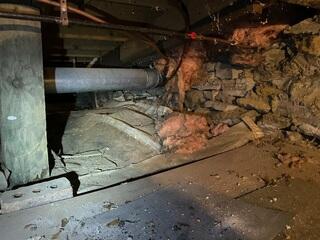 The basement and crawl space show signs of moisture intrusion, deteriorating insulation, and rodent activity. Damaged pink insulation and exposed stone walls reveal years of neglect, contributing to high energy bills and pest issues.