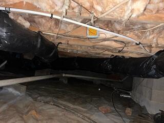 In this first image, the crawl space shows clear symptoms of long-term moisture issues. The insulation is falling from the joists, the ground liner is thin and torn, and exposed ductwork is vulnerable to condensation. These conditions allow humid air to rise into the home, causing musty odors, sagging floors, and higher energy bills.