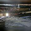This photo shows the crawl space before work began. The black vapor barrier is loosely laid and wrinkled, with insulation hanging from the ceiling joists. Ductwork runs throughout the space, but the overall condition looks messy and unprotected, leaving the home vulnerable to moisture and pests.