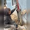 A Saber Foundation & Concrete Repair technician installs a foundation pier alongside a San Diego home. The pier system is designed to stabilize the settling foundation by transferring the structure's weight to stronger load-bearing soil below.
