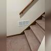 A white ventilation grille installed along the stair landing to help circulate air through the basement area.