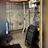 The PVC extraction pipe enters through the basement floor and runs vertically along the foundation wall, connecting the collection point beneath the slab to the exterior system.