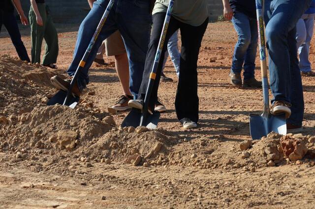 Digging the shovels into the dirt to break ground. 